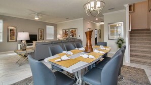 A dining area with a large table set for six, surrounded by six chairs. There is a modern chandelier above the table. - 9032hs-the Retreat at Championsgate (Davenport)