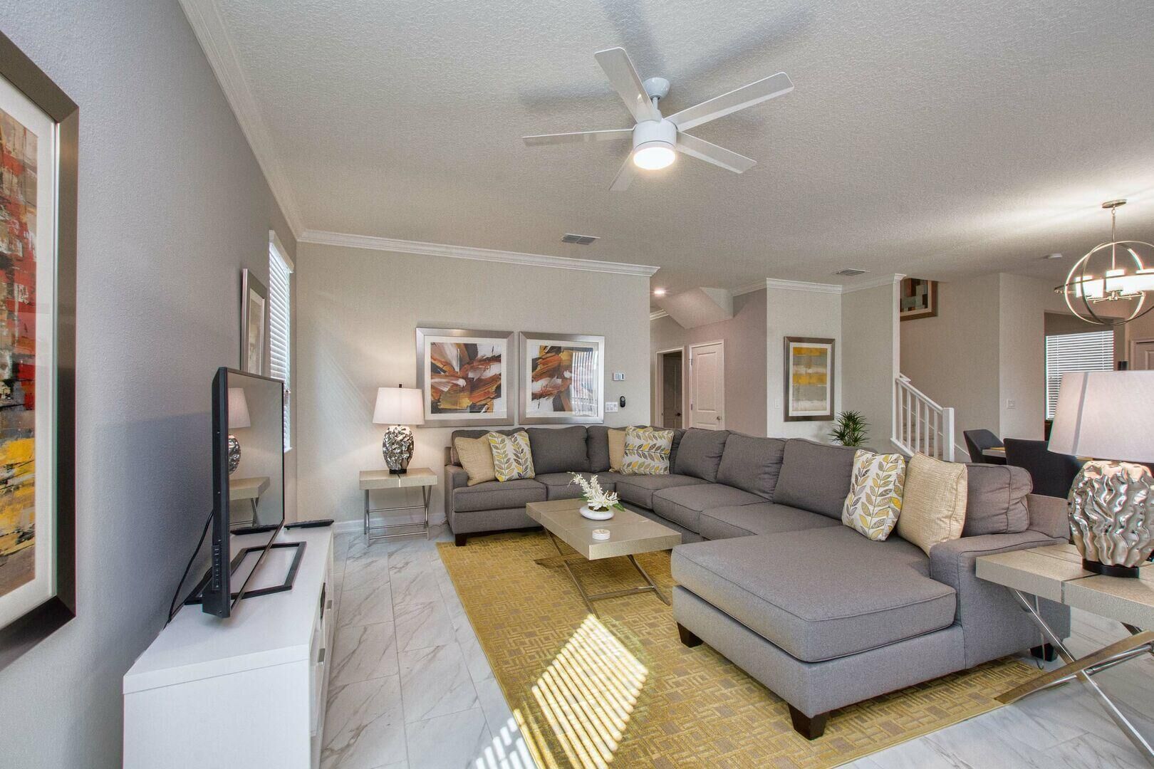 A modern living room with a sectional sofa, a flat-screen TV, and a ceiling fan.