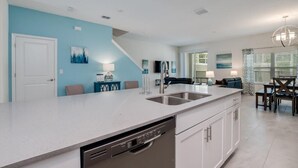 A modern kitchen with a dishwasher, a sink, and a dining area with a table and chairs. - C780pbd - The Retreat at Championsgate (Davenport)