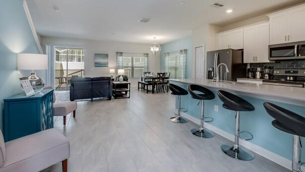 A modern kitchen with white cabinets, a black refrigerator, and a microwave. There is a dining area with a table and chairs. - C780pbd - The Retreat at Championsgate (Davenport)