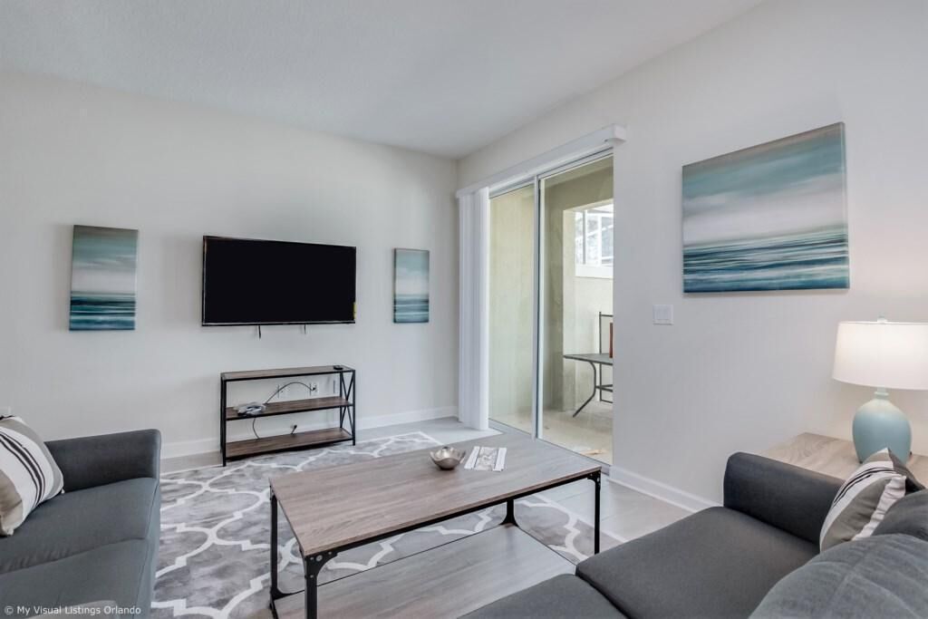 A modern living room with a flat-screen TV, grey sofas, a coffee table, and artwork on the walls.