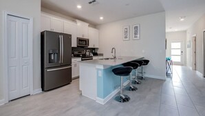 A modern kitchen with a central island, stainless steel appliances, and a bar area with stools. - C780pbd - The Retreat at Championsgate (Davenport)