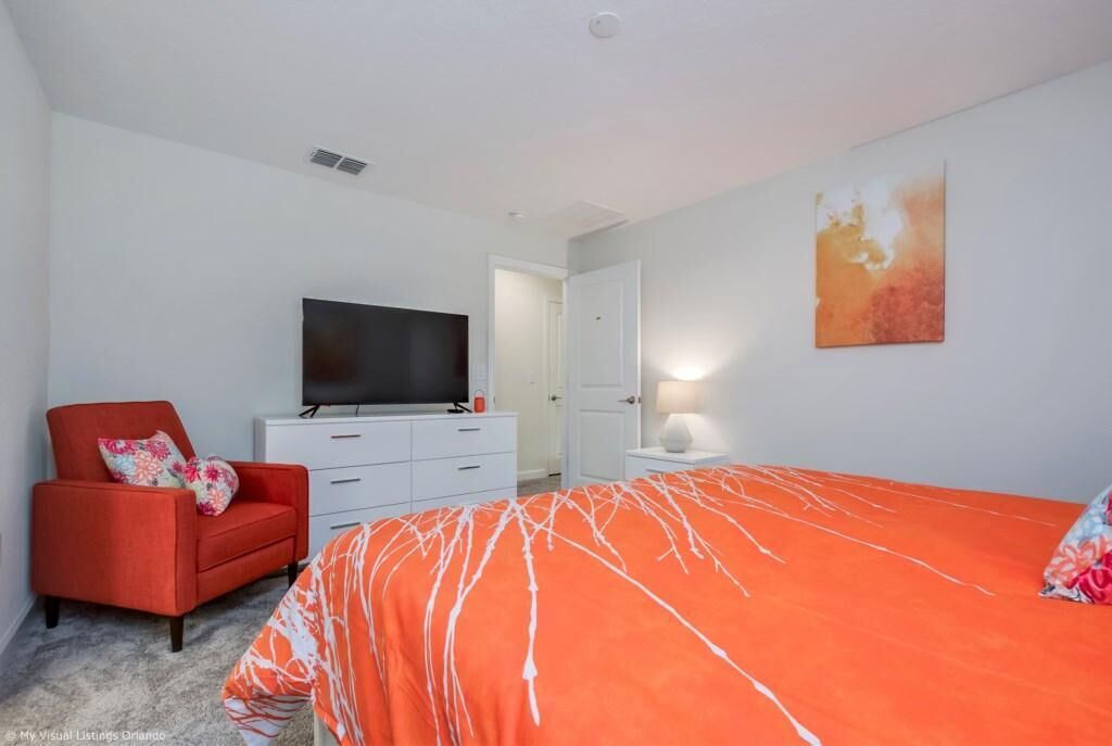 Ein Schlafzimmer mit einem großen Bett, einem roten Sessel, einem Fernseher und einem Bild an der Wand.