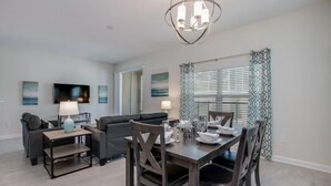 A modern living room with a dining area, featuring a chandelier, flat-screen TV, and artwork on the walls. - C780pbd - The Retreat at Championsgate (Davenport)