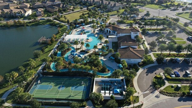 An aerial view of a residential area with a large swimming pool, tennis courts, and a lake. - 2404tgd Non Renting 11/28/2022 - Windsor at Westside (Kissimmee)