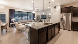 A modern kitchen with a large island, stainless steel appliances, and a dining area with a sofa and chairs. - 2404tgd Non Renting 11/28/2022 - Windsor at Westside (Kissimmee)
