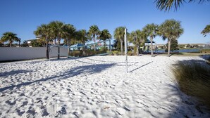 A sandy beach area with palm trees, a volleyball net, and a clear blue sky. - 2404tgd Non Renting 11/28/2022 - Windsor at Westside (Kissimmee)