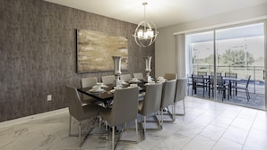 Un coin repas avec une table moderne dressée pour six personnes, une grande peinture abstraite accrochée au mur et une vue sur un patio à travers de grandes portes vitrées.