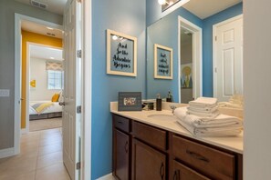 A bathroom with a large mirror, framed pictures on the wall, and a stack of towels on the counter.