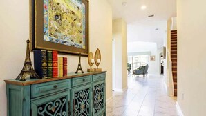 Un pasillo con un mueble azul verdoso, libros, objetos decorativos y un cuadro grande.