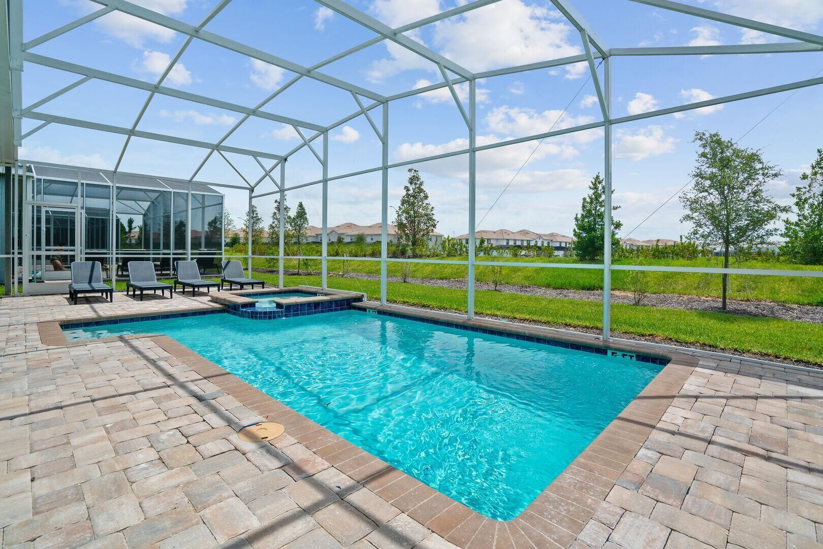 En swimmingpool med en glasvägg runt om, omgiven av en uteplats med solstolar och utsikt över ett bostadsområde.