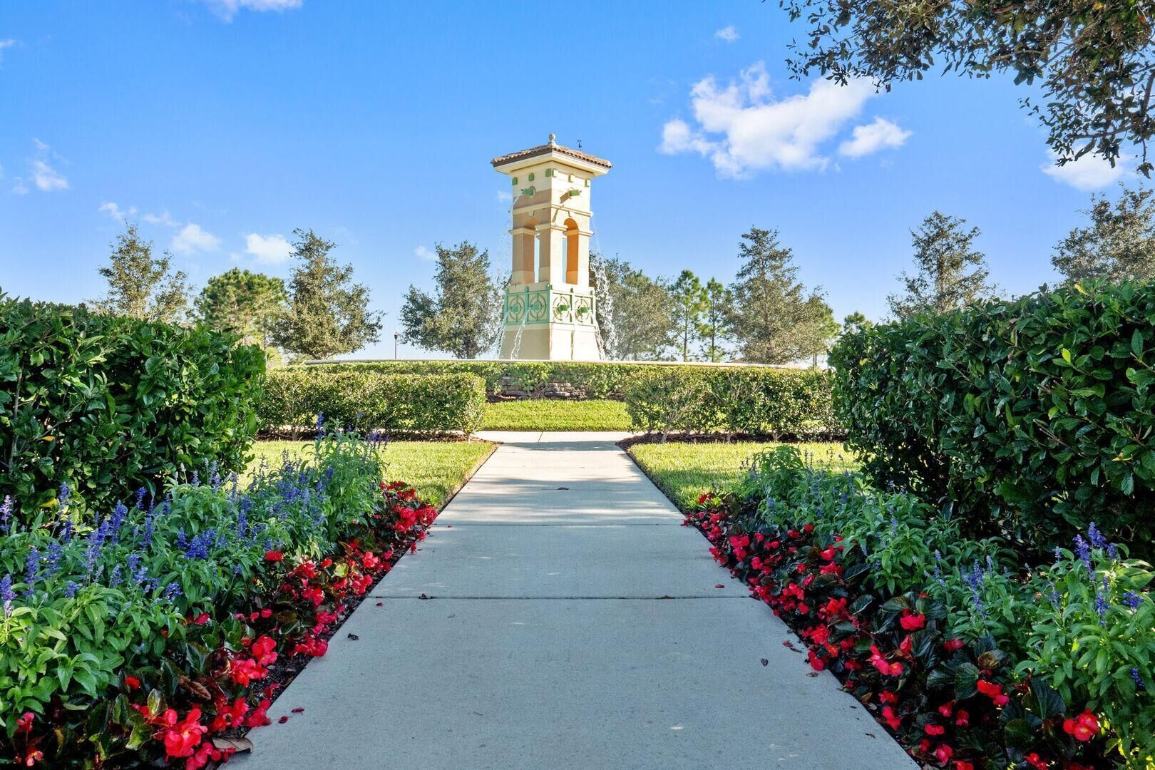 A garden pathway leading to a tall, freestanding structure with a tiled roof, surrounded by lush greenery and colorful flowers.