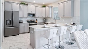 Una cocina moderna con armarios blancos, electrodomésticos de acero inoxidable y una isla central con taburetes de bar.