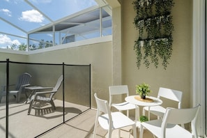 Eine sonnendurchflutete Terrassenanlage mit Glasveranda, weißen Stühlen, einem runden Tisch und hängenden Pflanzen.