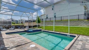A covered swimming pool with a clear blue water feature, surrounded by a patio area with lounge chairs and a small hot tub. - 1516fd-the Retreat at Championsgate (Davenport)
