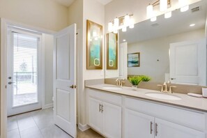 A modern bathroom with two sinks, a large mirror, and a door leading to a balcony.