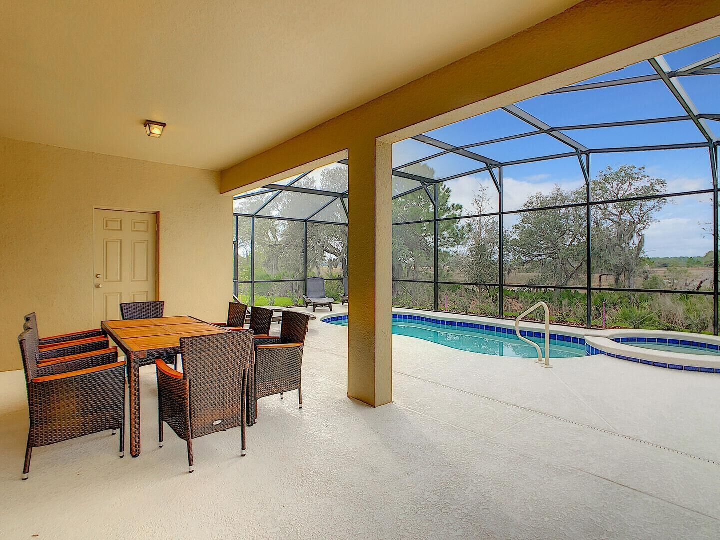 A covered patio area with a pool, a dining table with chairs, and a door.