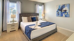 Una camera da letto con un letto grande, due comodini, un tavolino e una finestra con tende, oltre a un quadro appeso al muro.