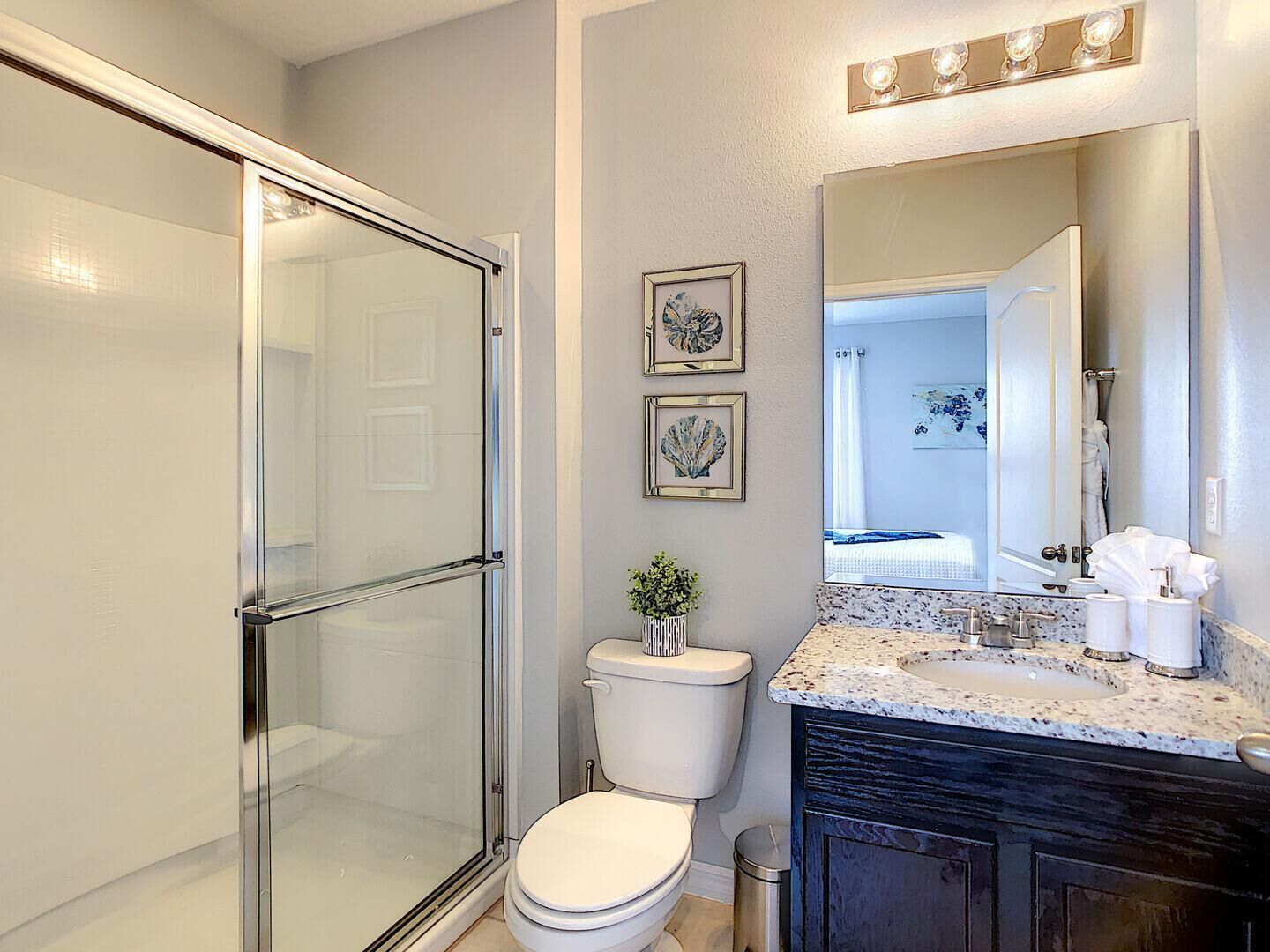 A modern bathroom with a glass shower enclosure, a toilet, a sink with a granite countertop, and a large mirror above the sink.