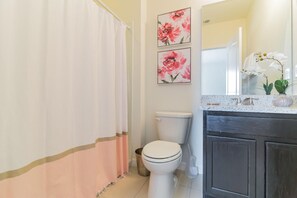 A bathroom with a toilet, a shower curtain, a sink with a mirror, and two floral wall art pieces.
