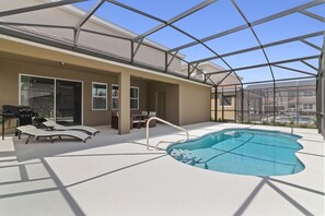 A covered outdoor swimming pool with lounge chairs and a barbecue grill.