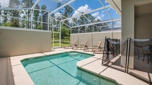 A covered outdoor swimming pool with clear blue water, surrounded by lounge chairs and a glass enclosure.