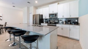 A modern kitchen with white cabinets, stainless steel appliances, and a central island with bar stools.