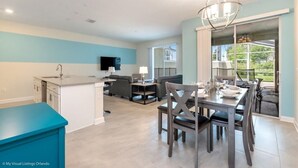 A modern kitchen with a blue countertop, a dining area with a table set for four, and a view of the outdoors through a large window.