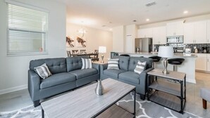 A modern living room with a grey sectional sofa, a coffee table, and a dining area with a chandelier.