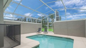 A swimming pool with a glass enclosure, two lounge chairs, and a view of trees and sky. - C550pbd- The Retreat at Championsgate (Davenport)