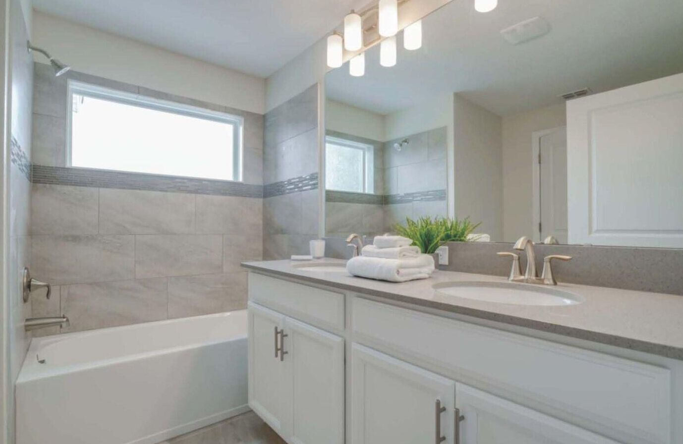 A modern bathroom with a bathtub, two sinks, and a large mirror.