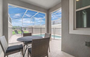Une terrasse extérieure avec une table ronde et des chaises en osier, donnant sur une piscine et un ciel dégagé.