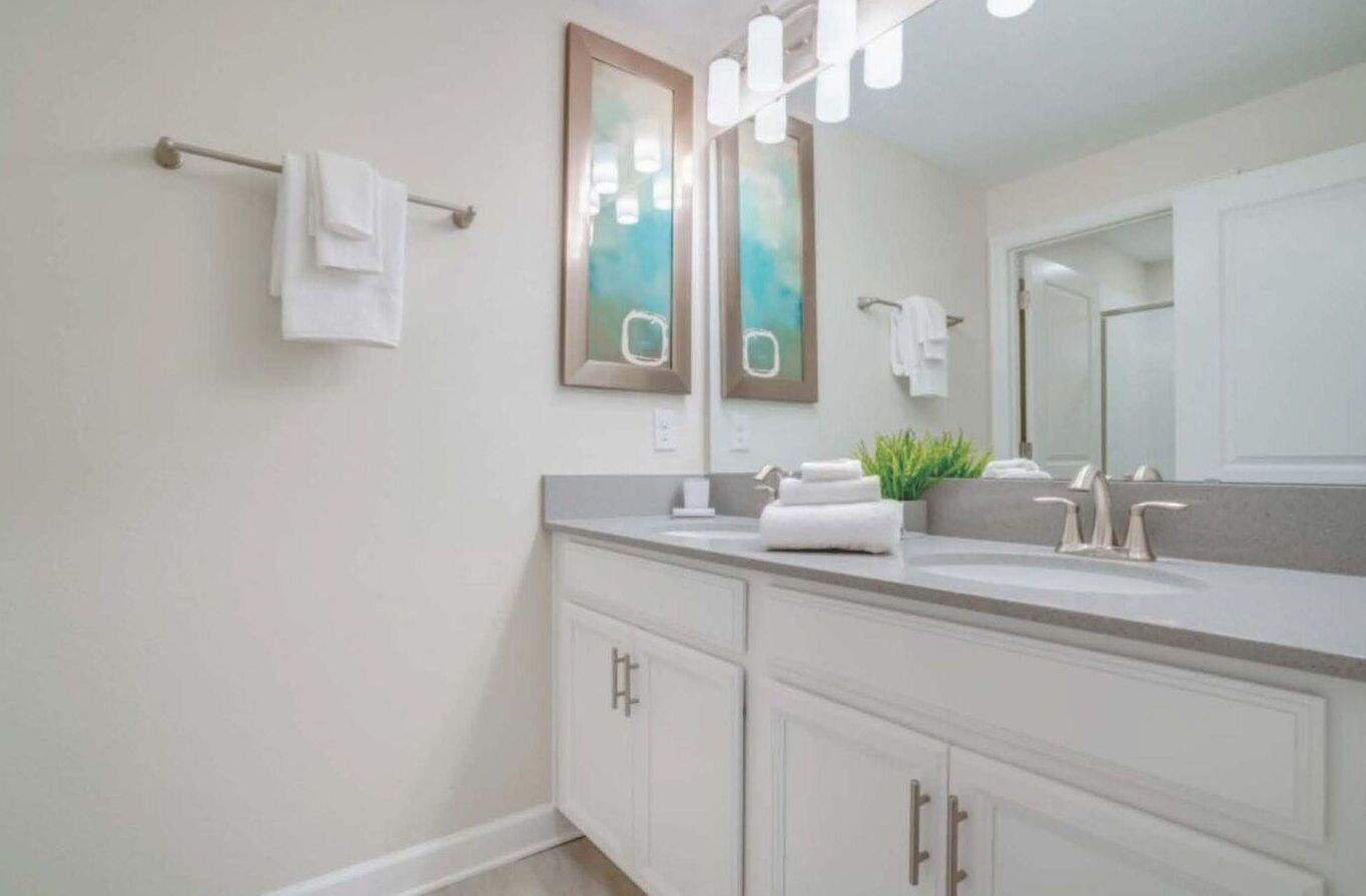 Une salle de bain moderne avec un grand miroir, deux lavabos et un porte-serviettes.