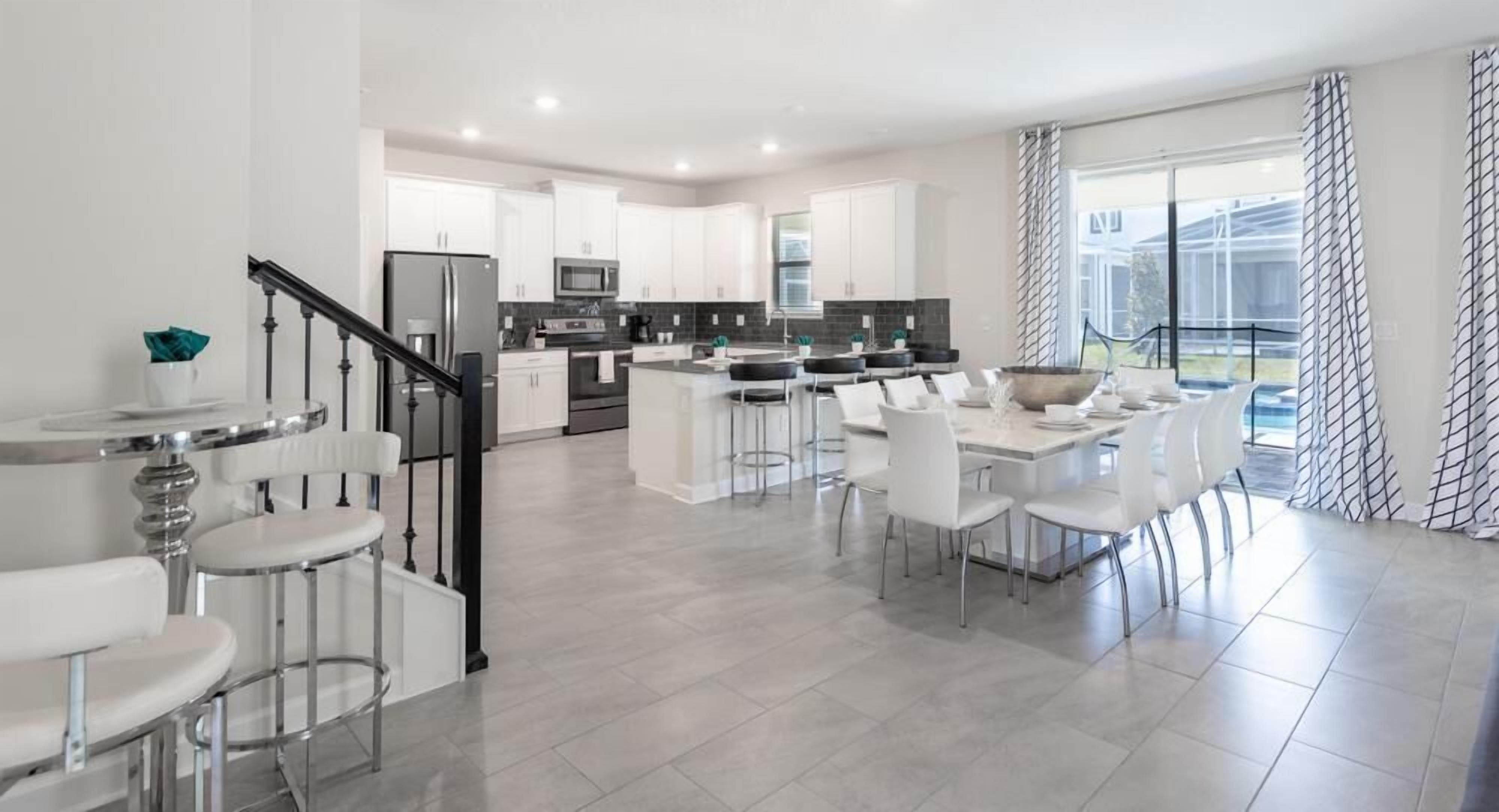 A modern kitchen with white cabinets, a central island, and a dining area with white chairs.