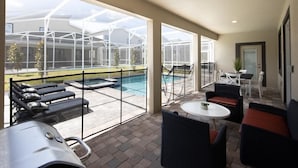 A covered outdoor area with a pool, lounge chairs, and a grill. - 720dsd-the Retreat at Championsgate (Kissimmee)
