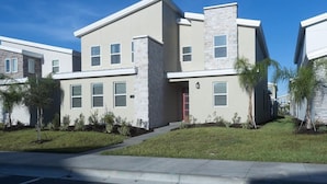 A modern two-story residential building with a stone facade, multiple windows, and a small front yard with landscaping. - 720dsd-the Retreat at Championsgate (Kissimmee)
