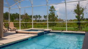 A covered outdoor swimming pool with lounge chairs and a view of a grassy area. - 801dsd-the Retreat at Championsgate (Kissimmee)