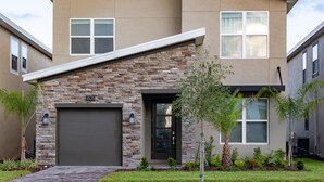 A modern two-story house with a stone facade, a garage, and a well-maintained front yard with small trees and shrubs. - 801dsd-the Retreat at Championsgate (Kissimmee)