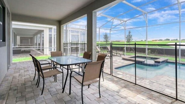 Un patio couvert, doté d’une structure en verre, une piscine et une table avec des chaises.
