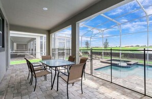 Een overdekt terrasgedeelte met glazen wanden, een zwembad en een tafel met stoelen.