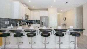 Une cuisine moderne avec des meubles blancs, un îlot central et un coin bar avec des tabourets.
