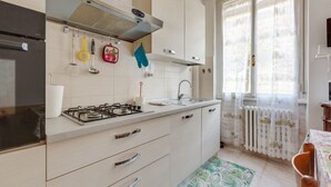 A kitchen with a gas stove, white cabinets, a window with curtains, and a patterned rug.