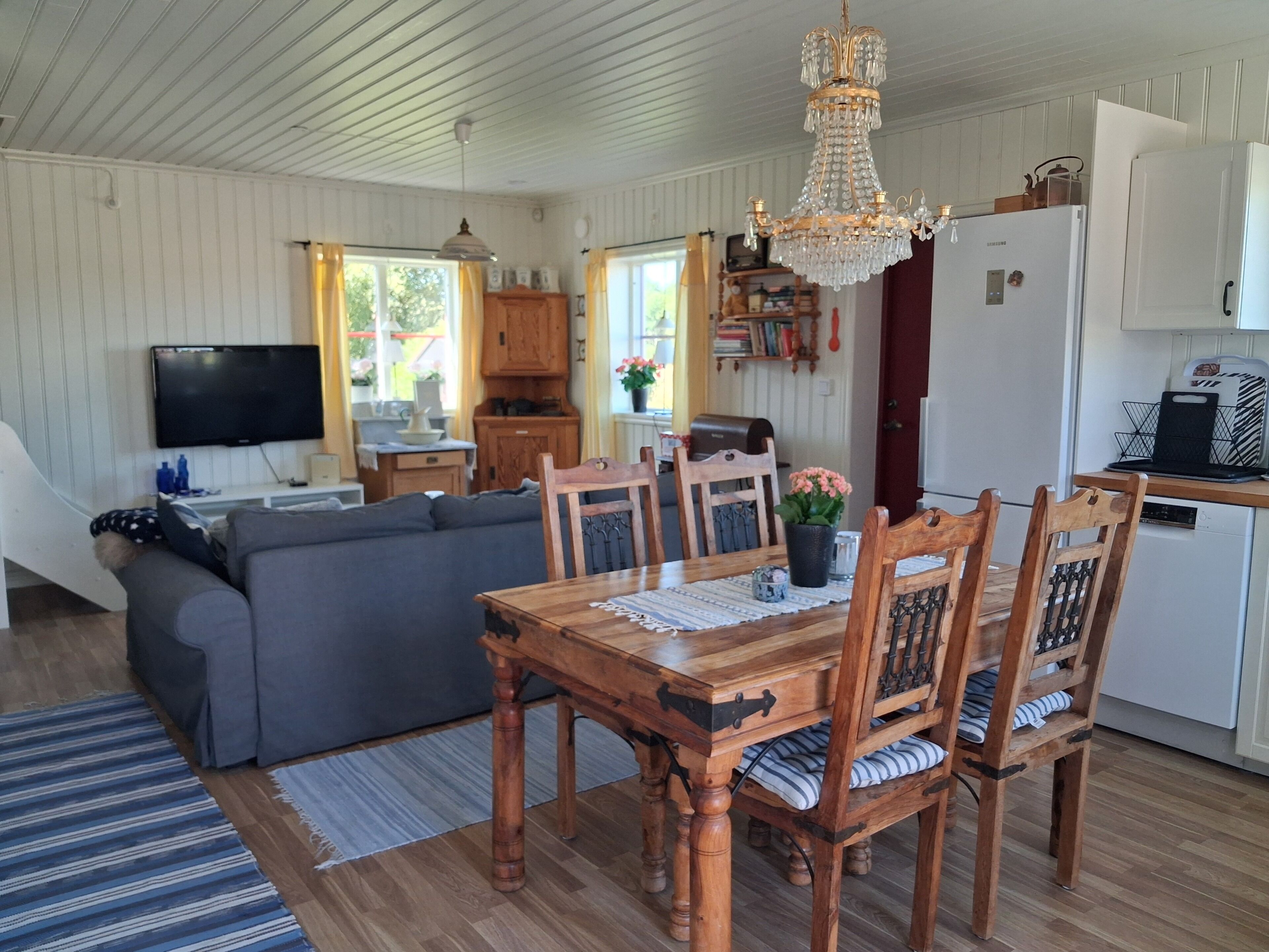 Una sala de estar acogedora con sofá, mesa de comedor y sillas, una zona de cocina con refrigerador y televisión.