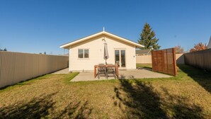 Une maison de plain-pied avec un patio, une petite table et des chaises, et une porte-fenêtre coulissante.
