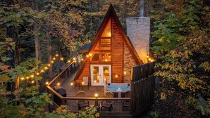 Een chalet met een stenen schoorsteen, houten terras en lichtslingers.