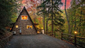 Een stenen chalet met een puntig dak, een houten terras en een stenen muur rondom het terrein.