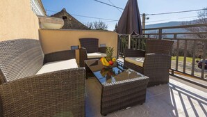 Un balcon agrémenté de meubles en osier, une table en verre avec des fruits, et une vue sur les environs.
