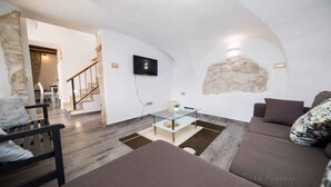 Un salon moderne avec un mur en pierre, une table basse en verre, un canapé et un téléviseur fixé au mur.