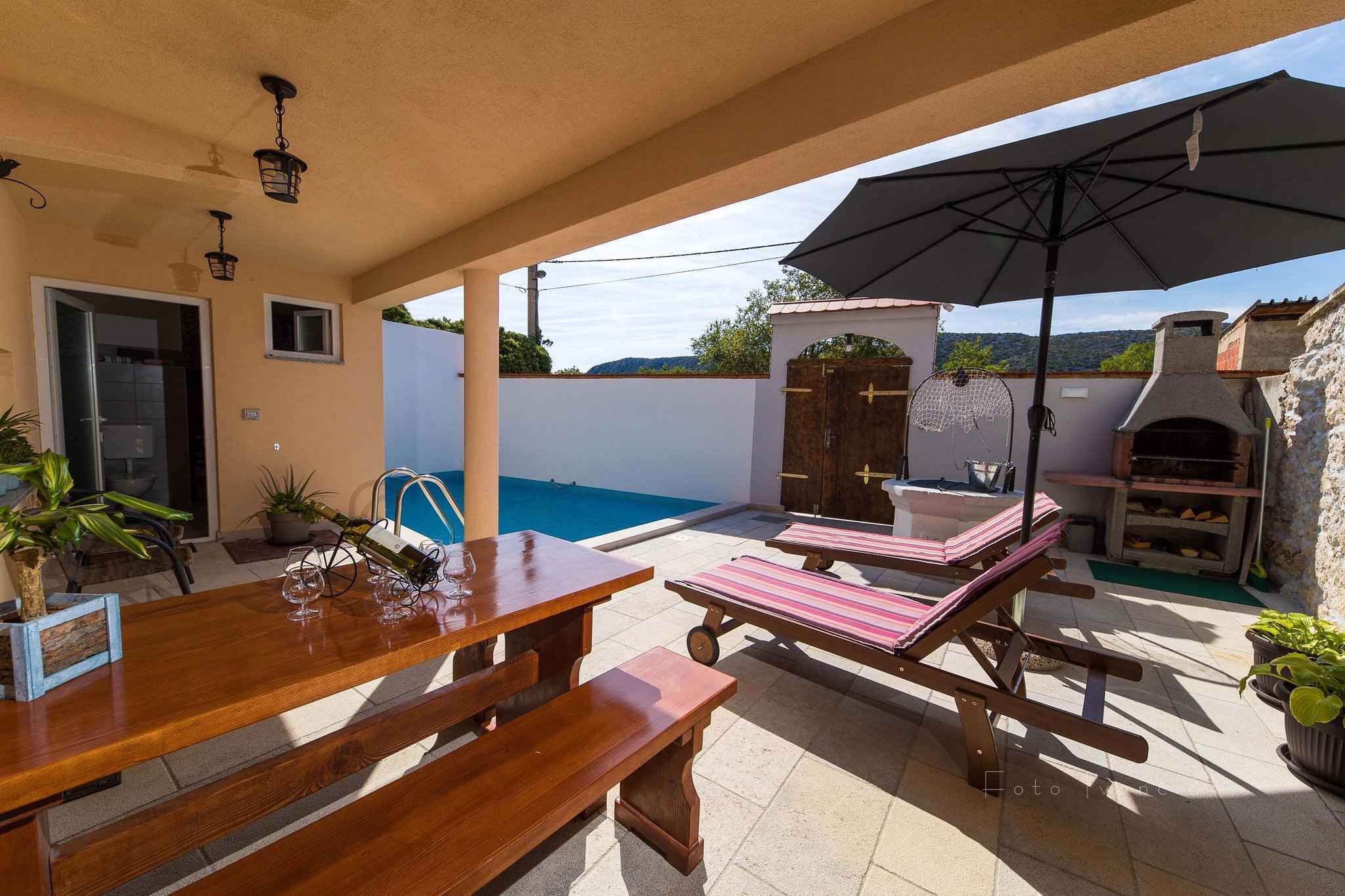 Un espace patio avec une piscine, des chaises longues, une table en bois et un barbecue.