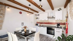 Une cuisine moderne avec des meubles blancs, un plan de travail noir et un coin repas comprenant des chaises blanches et une table en verre.